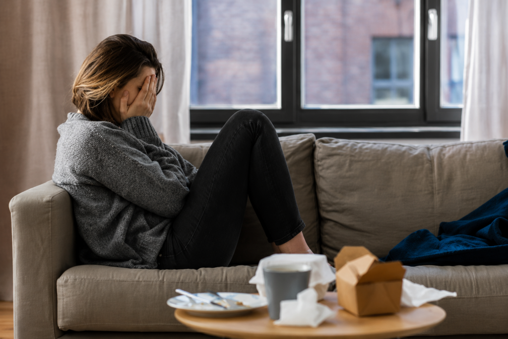 A woman on her sofa with her face in her hands, looking tearful