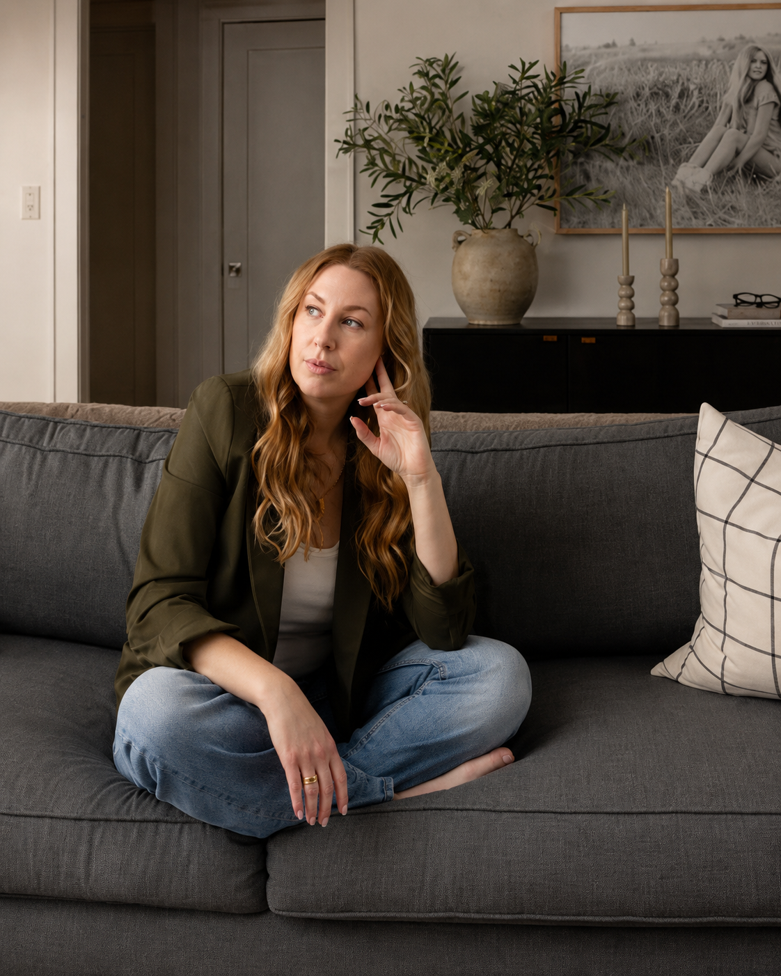 A woman sitting calmly on her couch, looking thoughtful in warm natural light